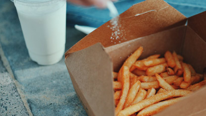 Papas fritas en un recipiente de cartón siendo saladas.