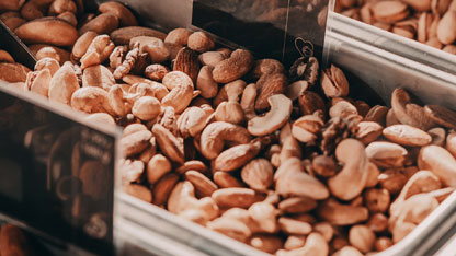 Un primer plano de nueces surtidas, incluyendo anacardos, almendras y nueces, expuestas en un recipiente de metal.