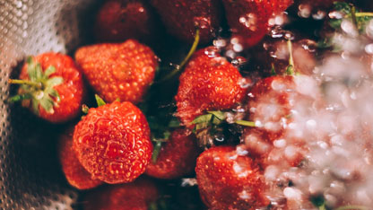 Primer plano de fresas siendo enjuagadas bajo agua corriente en un colador.