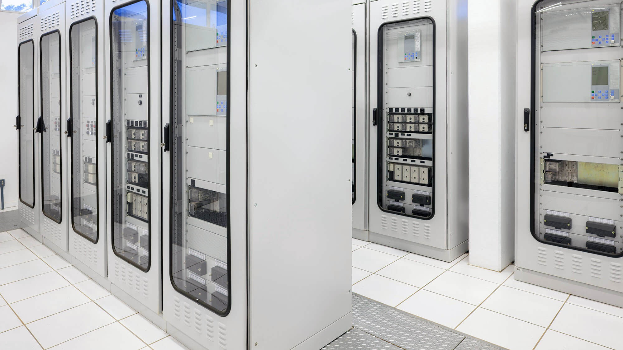 A clean and organized electric room features rows of specialized control panels and protection relay cabinets in an electrical substation. 