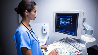 Medical professional operating an ultrasound machine with imaging displayed on the monitor.